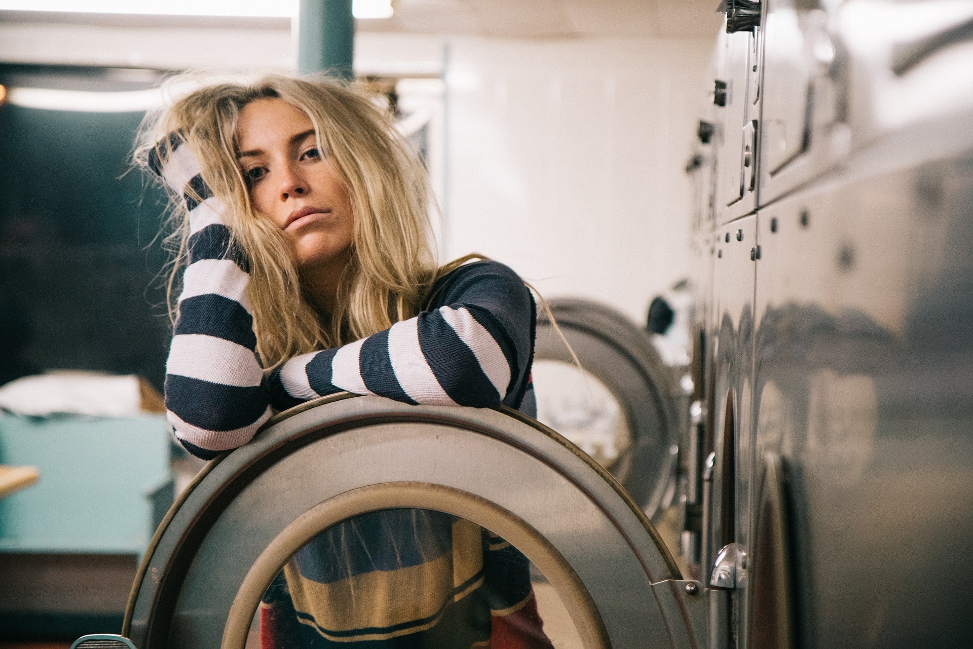 uma rapariga empoleirada na porta de uma máquina de lavar roupa self-service