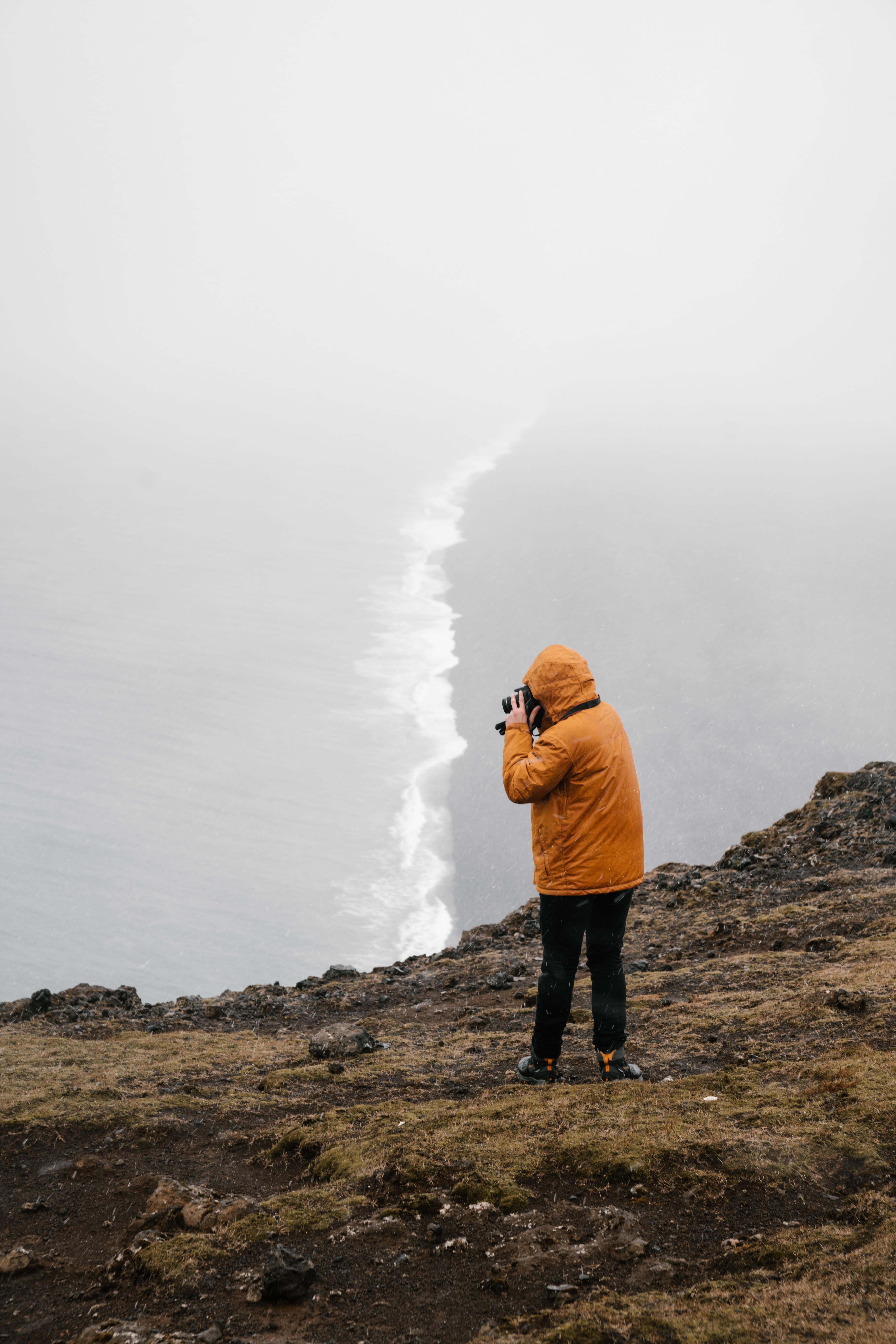 uma pessoa com um impermeável vestido a tirar foto ao mar revolto da tempestade